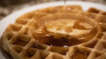 A waffle with syrup being poured onto it.