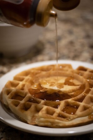 A waffle with syrup being poured onto it.