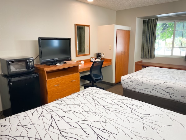 Habitación de hotel con cama, escritorio con ordenador, microondas y armario.