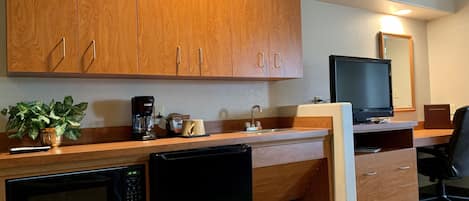 A compact kitchen with wooden cabinets, a microwave, a coffee maker, a sink, and a television.