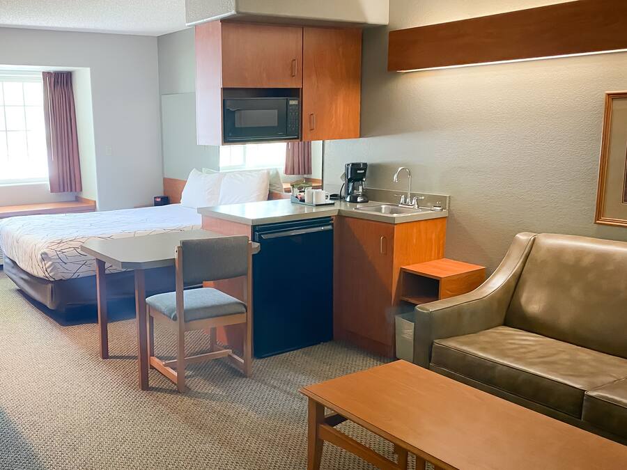 Habitación de hotel compacta con una cama, una kitchenette pequeña, un comedor y una zona de estar.