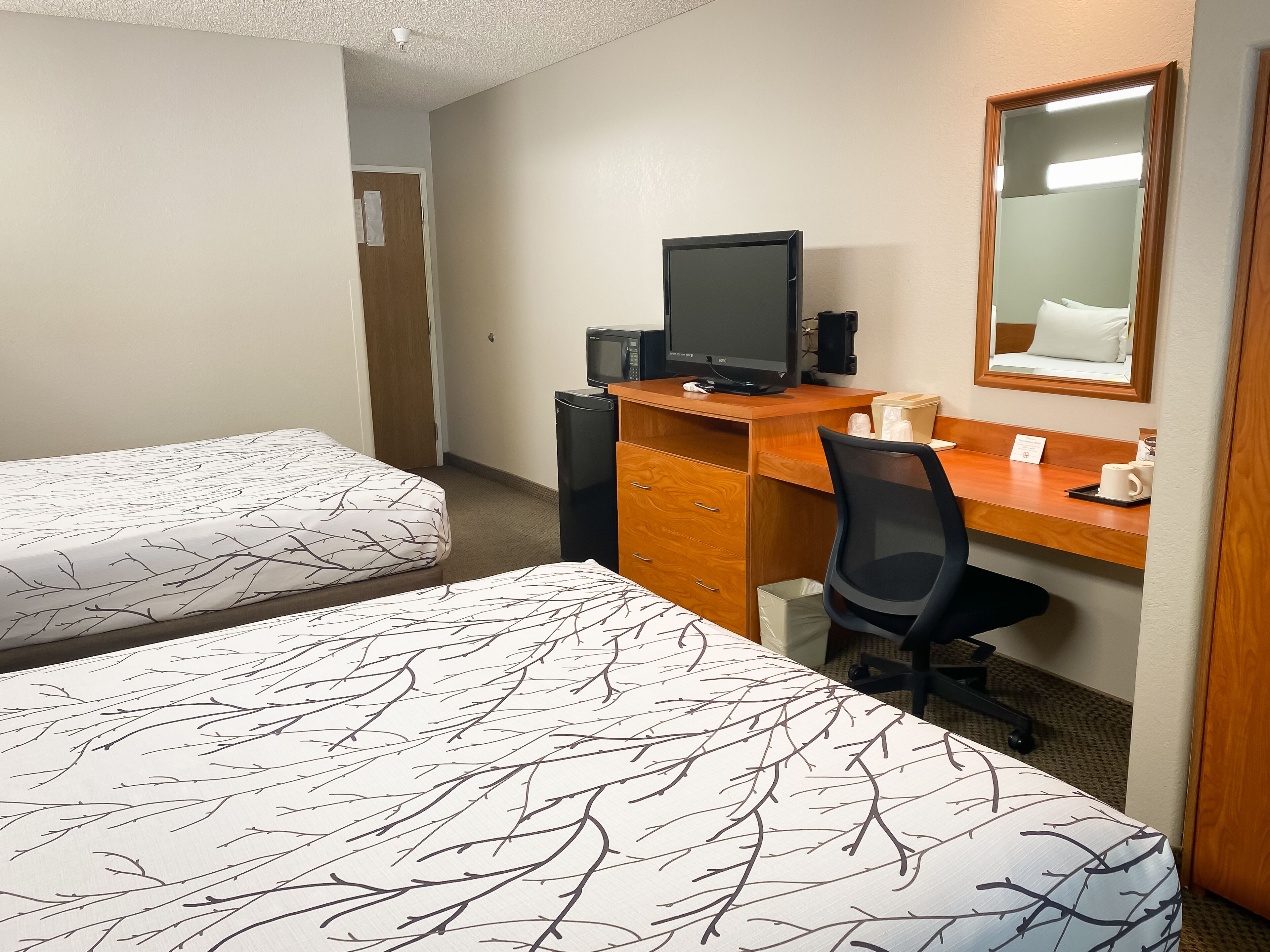 A hotel room with two beds, a desk with a computer, a chair, and a mirror.