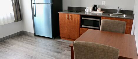 A compact kitchen with a refrigerator, microwave, and sink. There is a dining table with chairs.