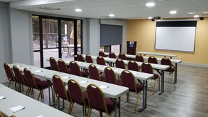 Un salón de conferencias con filas de mesas y sillas, una pantalla de proyector y un atril.