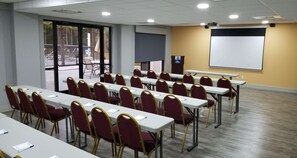 Un salón de conferencias con filas de mesas y sillas, una pantalla de proyector y un atril.