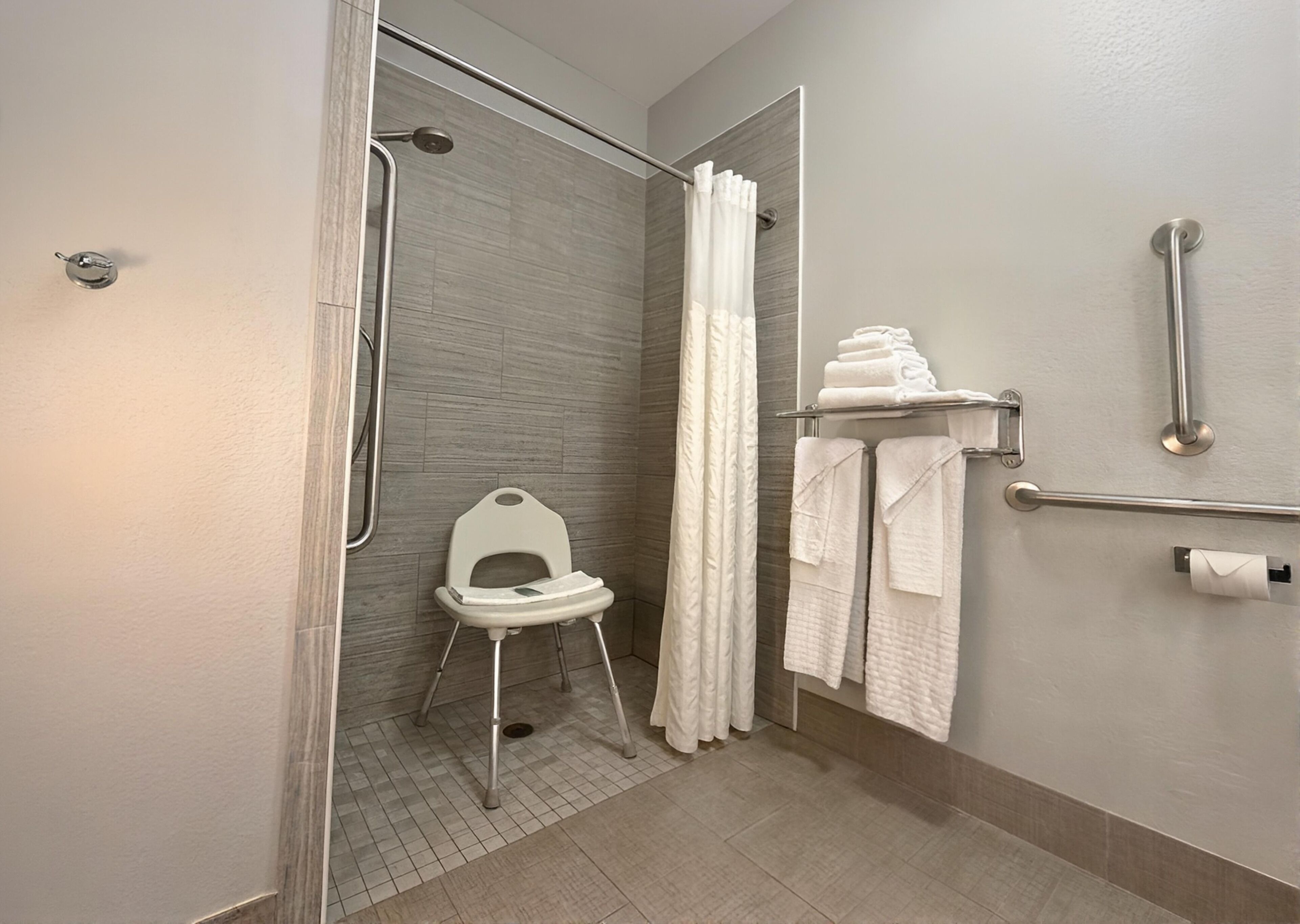 A bathroom with a shower, a toilet with a raised seat, a grab bar, and a towel rack.