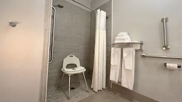 A bathroom with a shower, a toilet with a raised seat, a grab bar, and a towel rack.