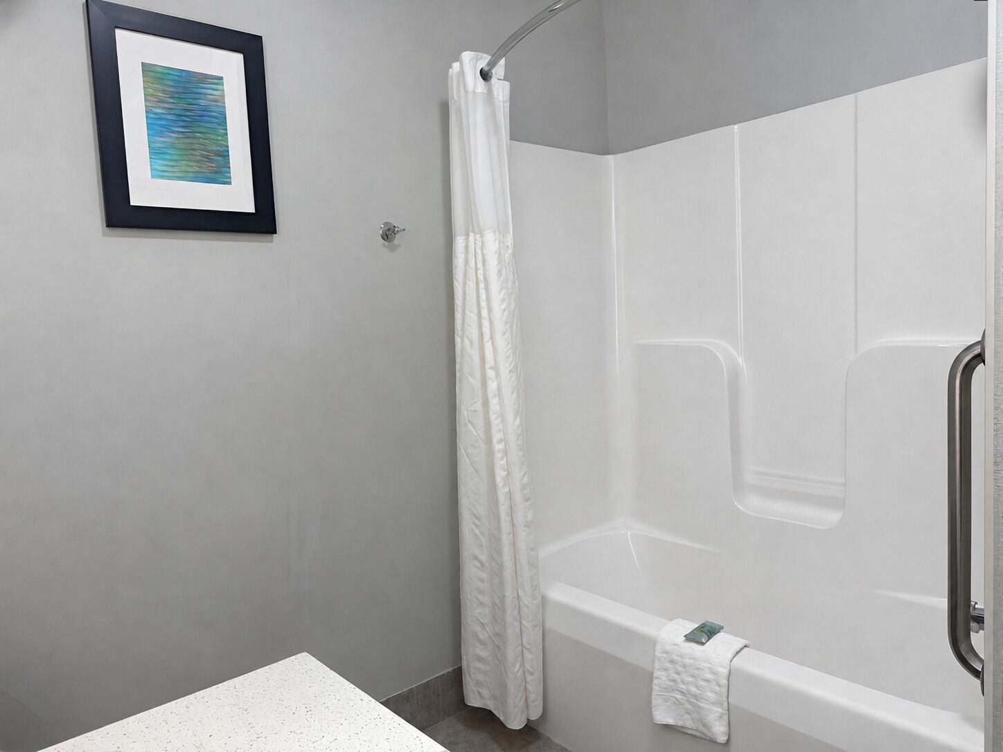 A modern bathroom with a shower, a framed picture on the wall, and a towel on the bathtub.