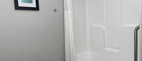 A modern bathroom with a shower, a framed picture on the wall, and a towel on the bathtub.