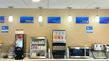 Un área de comida autoservicio con diferentes dispensadores de bebidas, un microondas y un refrigerador.