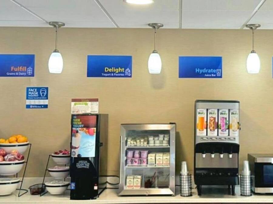A self-service food station with various drink dispensers, a microwave, and a refrigerator.
