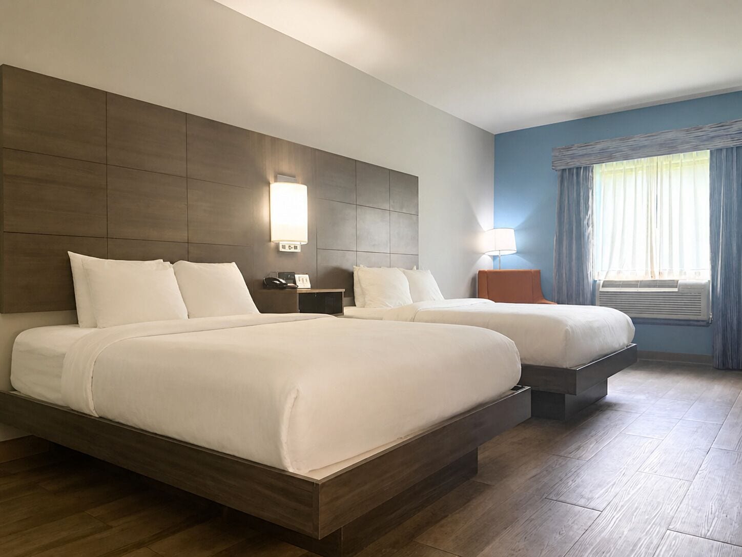 Habitación de hotel con dos camas, una mesita de noche, una lámpara y una ventana con cortinas.