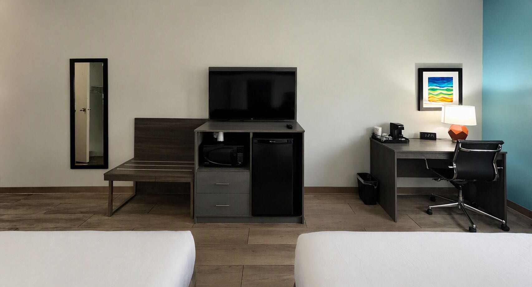 A hotel room with two beds, a desk with a computer, a TV, and a small kitchenette.