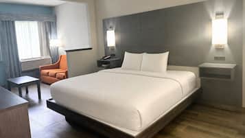 A hotel room with a large bed, bedside tables, a desk, an orange chair, and a view of the outdoors.