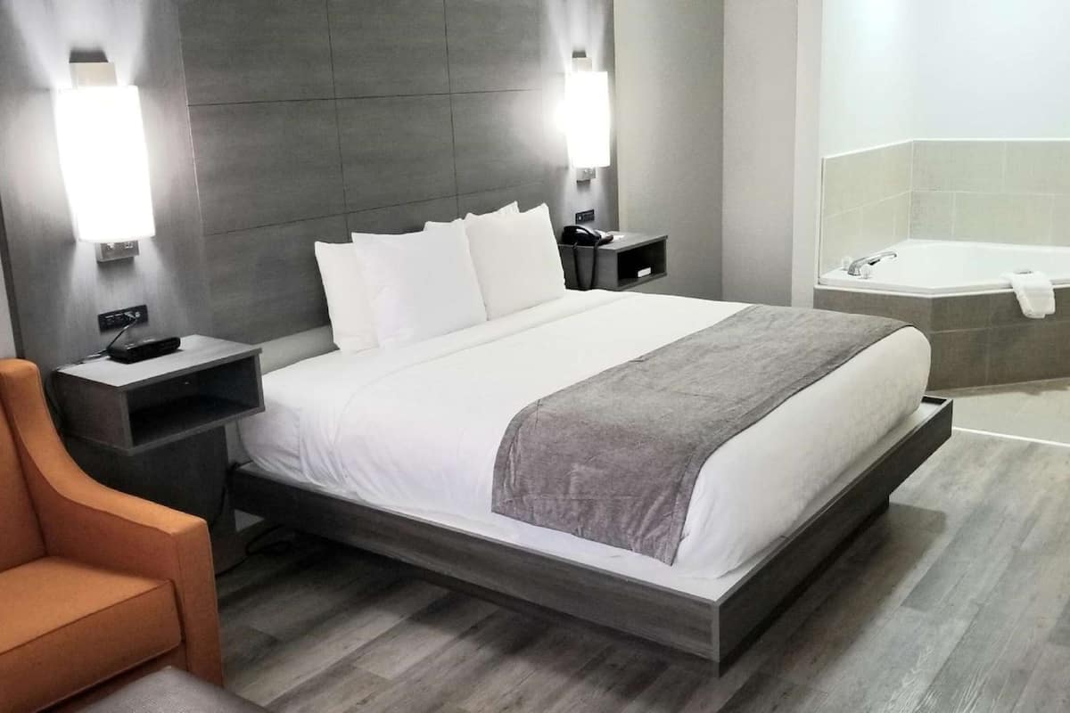 Una habitación de hotel moderna con una cama grande, mesitas de noche, una silla, un baño con bañera y ducha.