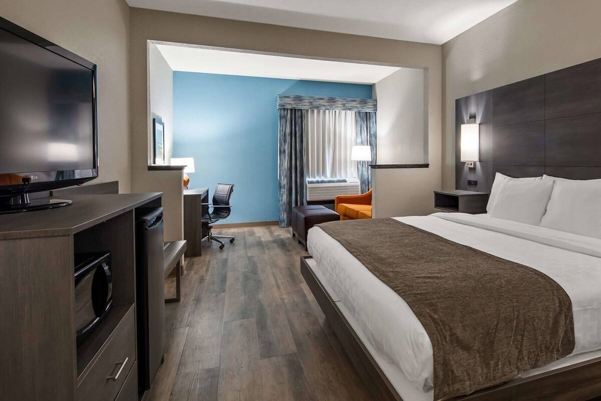 Una habitación de hotel con cama, escritorio, televisión y ventana con cortinas.