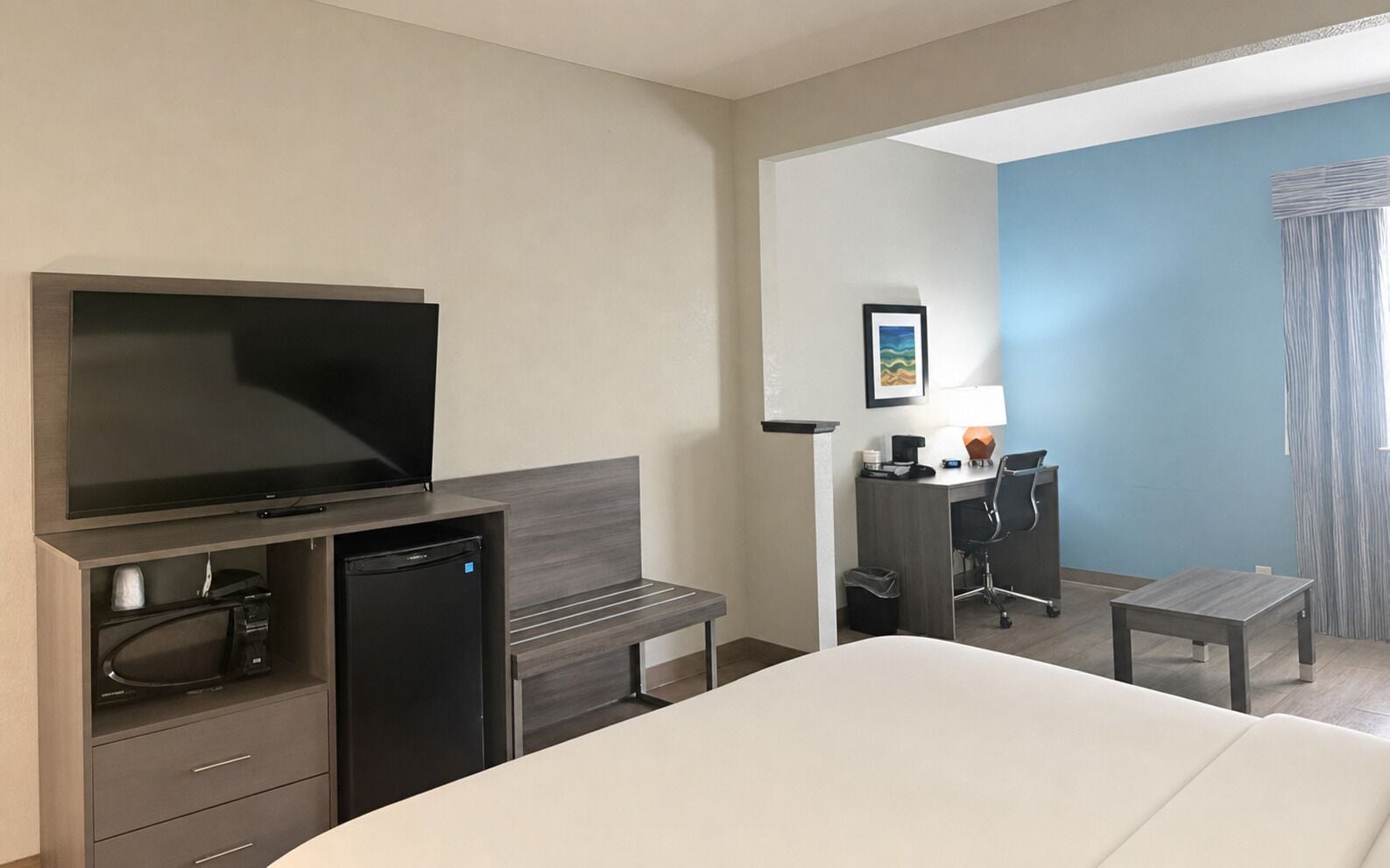 Una habitación de hotel con cama, televisión, escritorio con silla y una mesita.