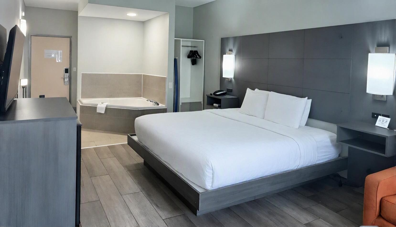 A modern hotel room with a large bed, a separate bathroom with a bathtub, a desk, and a chair.
