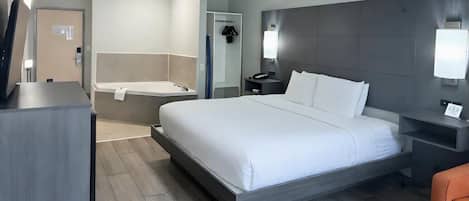 A modern hotel room with a large bed, a separate bathroom with a bathtub, a desk, and a chair.