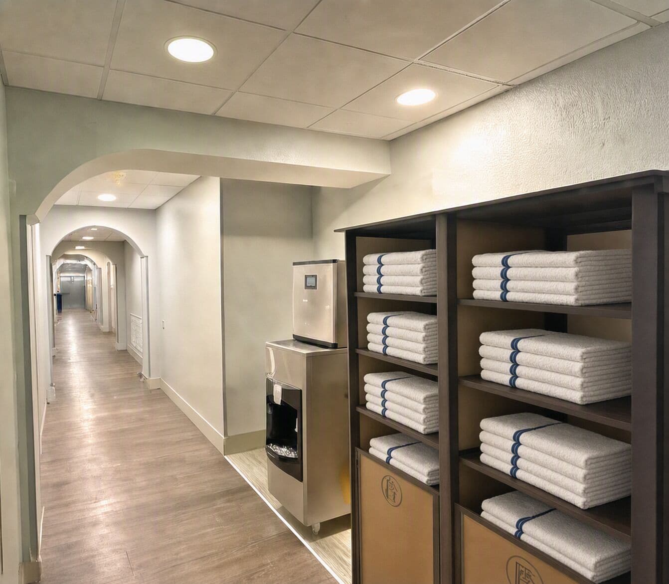 Un couloir d’hôtel avec un comptoir de réception, un kiosque en libre-service et des étagères remplies de serviettes pliées.
