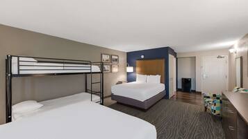 A hotel room with a bunk bed, a single bed, a desk, and a small seating area.