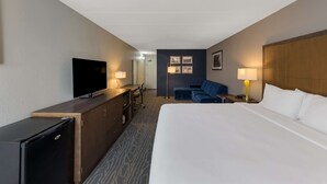 A hotel room with a large bed, a desk with a television, a small refrigerator, a sofa, and a nightstand with a lamp. - Comfort Inn & Suites Tipp City Dayton North I-75 (Tipp City)