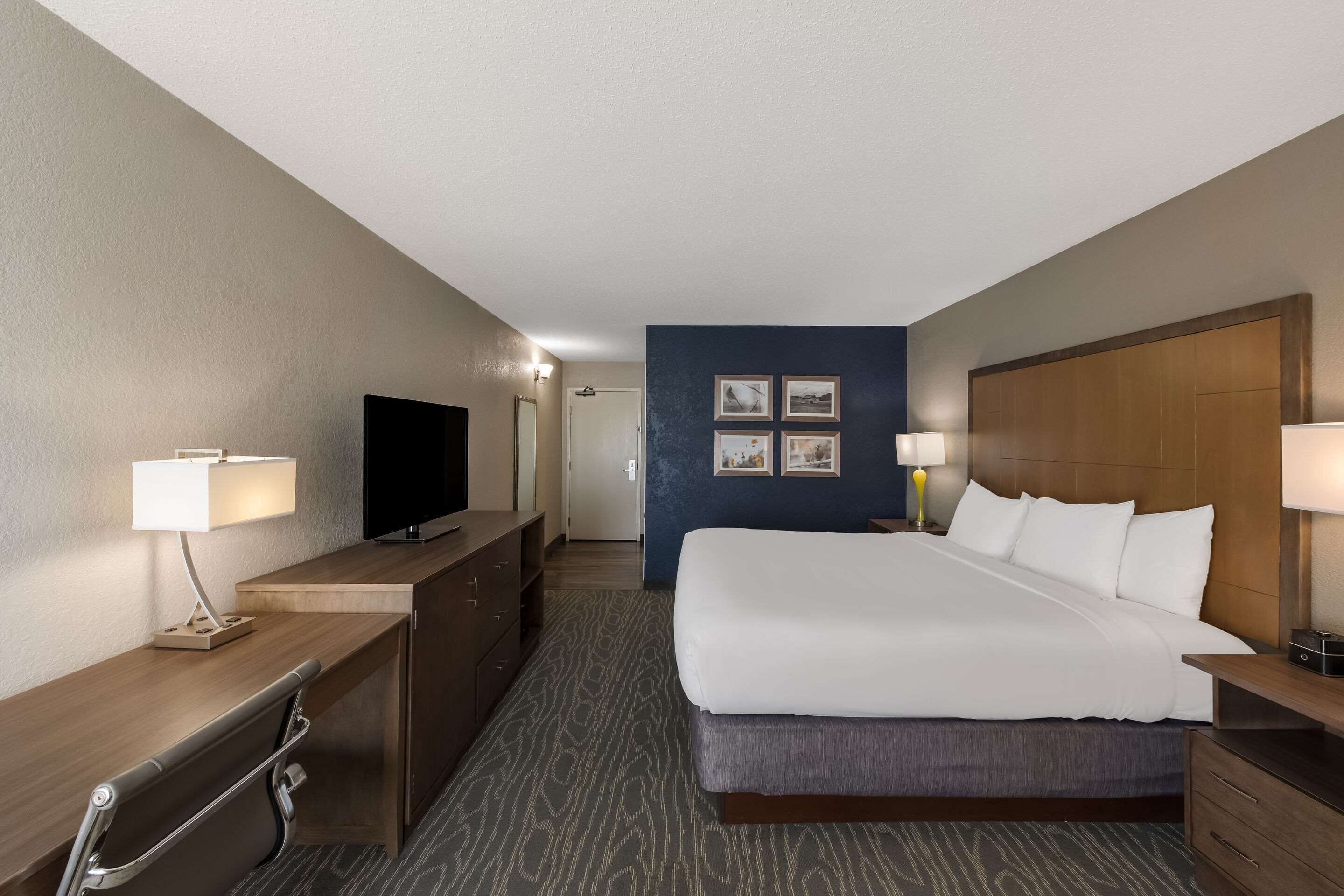 A hotel room with a bed, bedside tables, a desk with a lamp, a television, and a headboard.