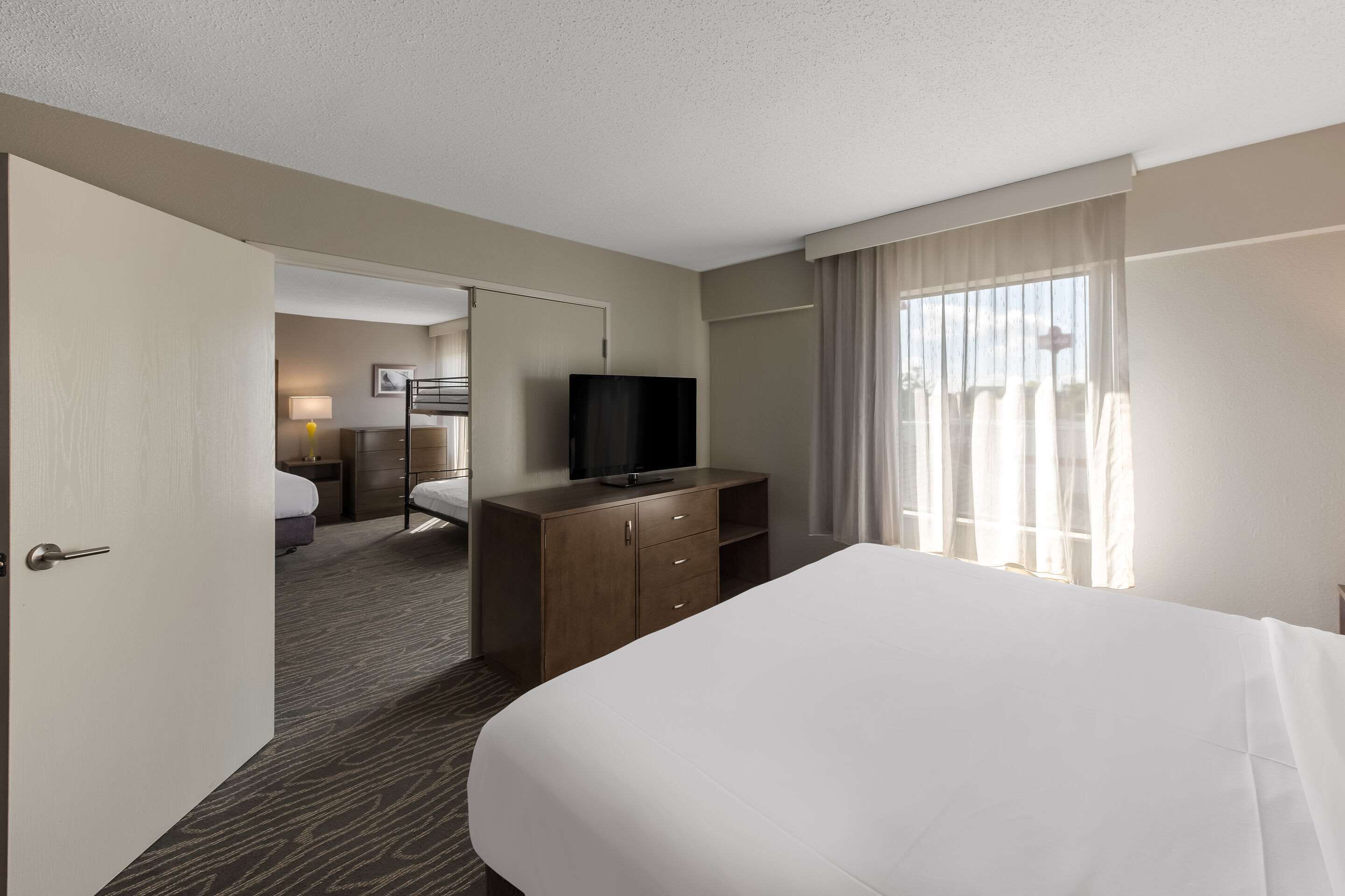 A hotel room with a large bed, a wooden dresser, a television, and a door leading to another room.