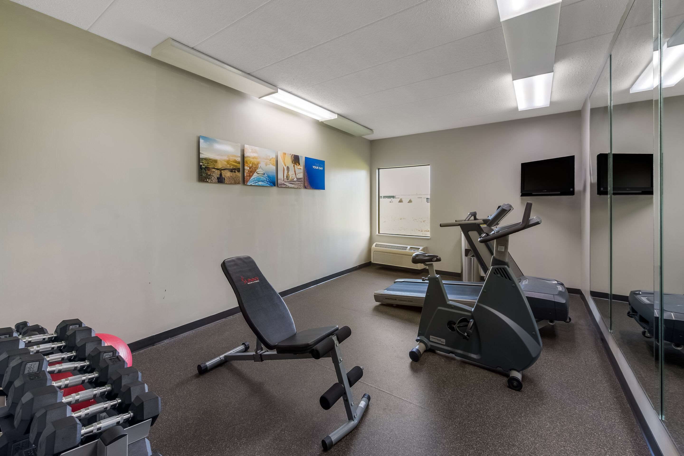 Ett gym med träningsutrustning, inklusive hantlar, en träningsbänk, löpband och en motionscykel.