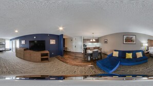 A panoramic view of a hotel room with a curved ceiling, a blue sofa, a bed, a TV, and a dining area with a table and chairs. - Comfort Inn & Suites Tipp City Dayton North I-75 (Tipp City)