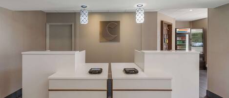 Zona de recepción de diseño moderno, con mostrador de recepción, dos lámparas colgantes, una obra de arte en la pared y un refrigerador con bebidas.
