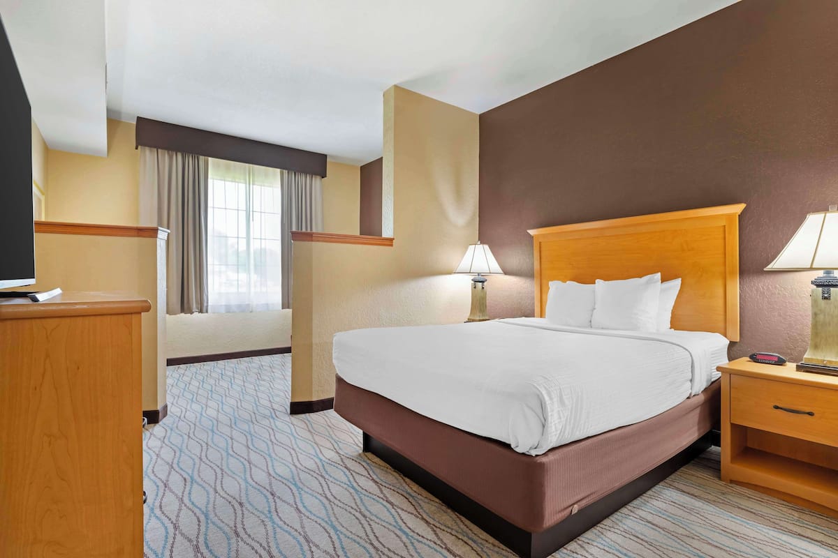 Ein Hotelzimmer mit einem großen Bett, Nachttischen, einem Schreibtisch und einem Fenster mit Vorhängen.