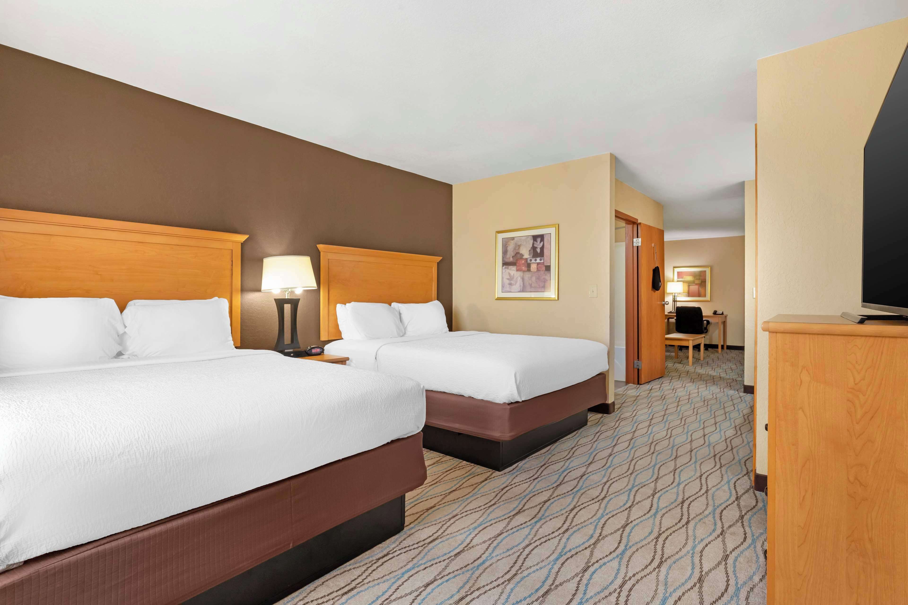 A hotel room with two beds, a desk, a chair, and a television.