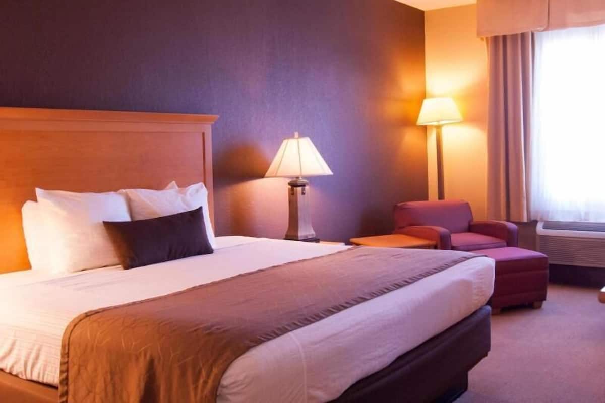 Ein Hotelzimmer mit einem großen Bett, zwei Nachttischlampen, einem Sessel und einem Fenster mit Vorhängen.