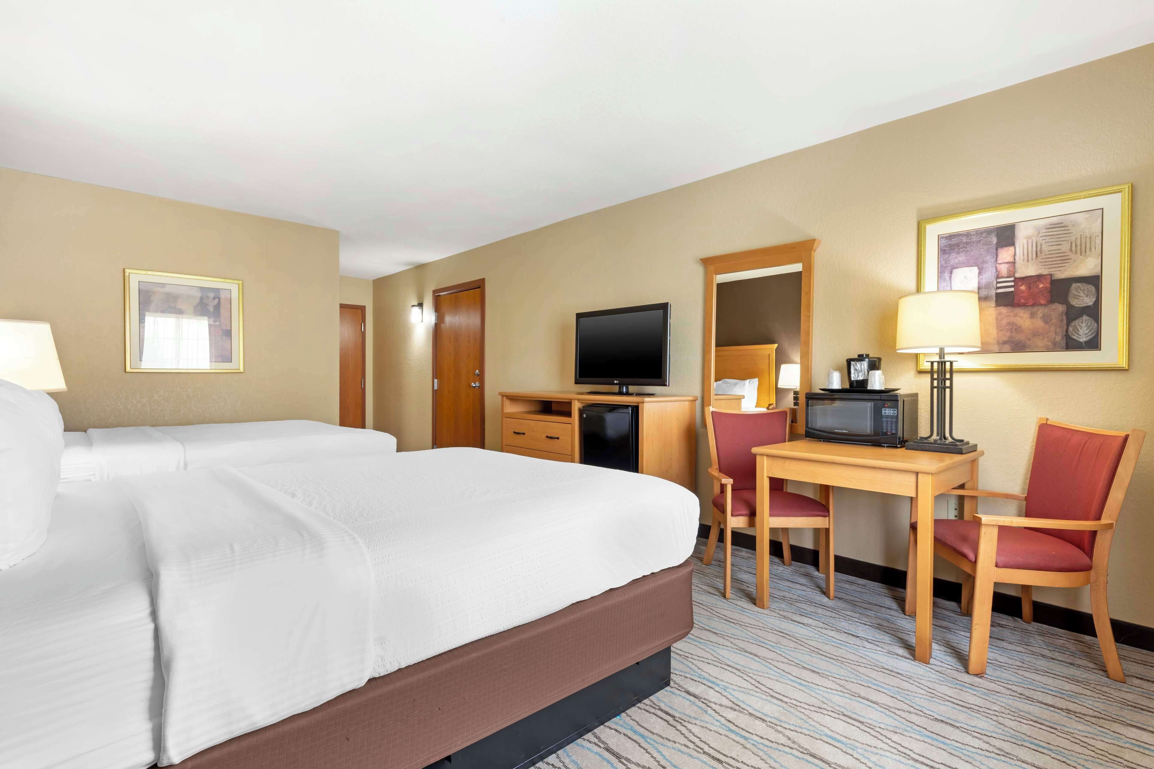 Ein Hotelzimmer mit einem großen Bett, einem Schreibtisch mit Stuhl, einem Fernseher und einer Mikrowelle.
