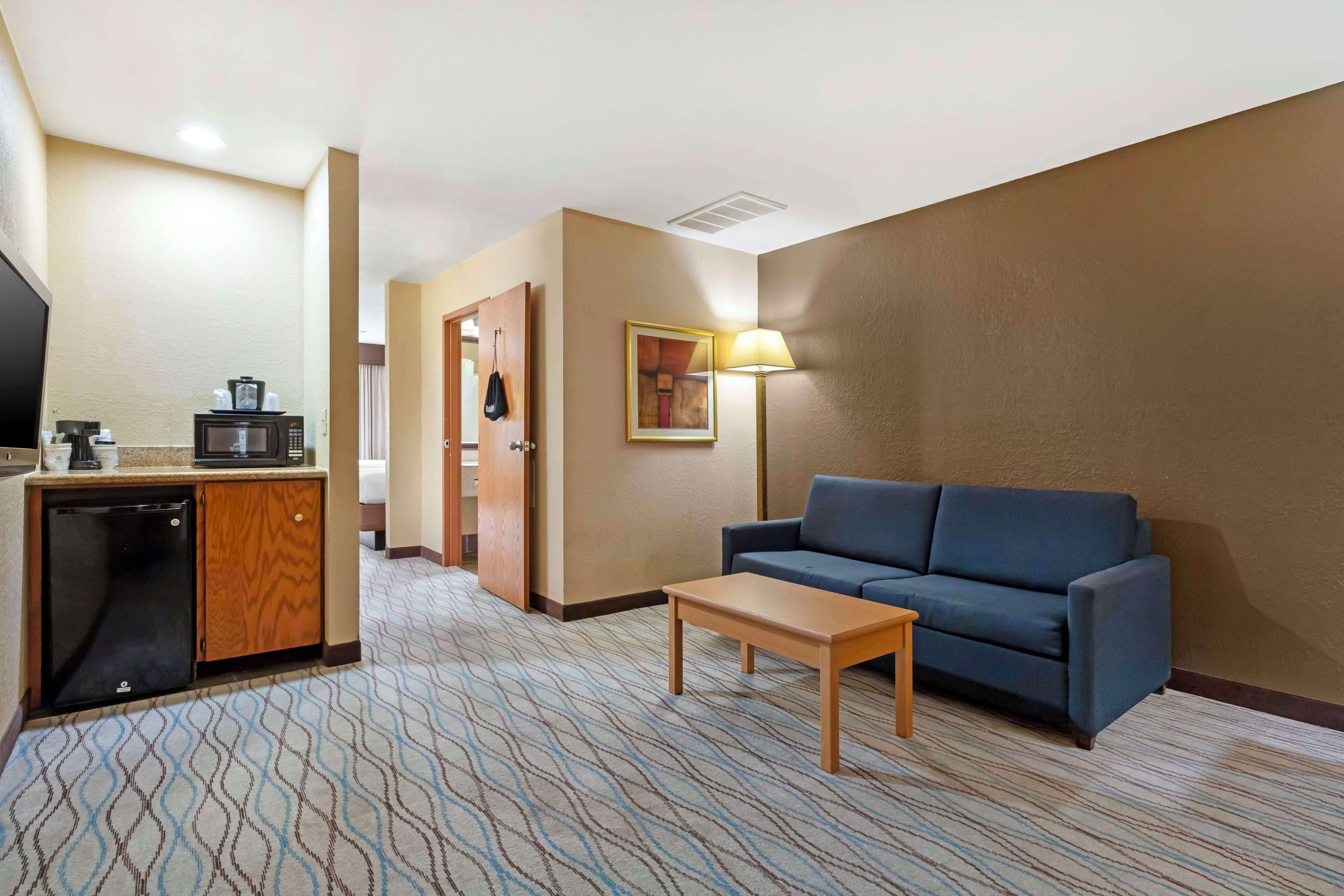 Ein Hotelzimmer mit Küchenzeile, einem blauen Sofa, einem Holztisch und einem gemusterten Teppich.