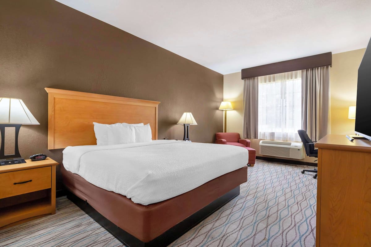 Ein Hotelzimmer mit einem großen Bett, Nachttischen, einem Schreibtisch, einem Stuhl und einem fenster mit Vorhängen.