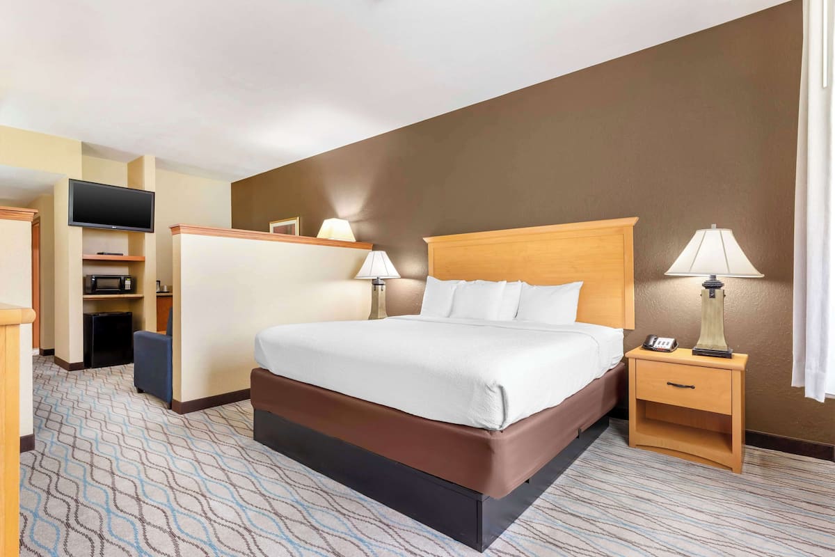 Ein Hotelzimmer mit einem großen Bett, einem Fernseher, einem Schreibtisch mit Lampe und einer kleinen Sitzecke.