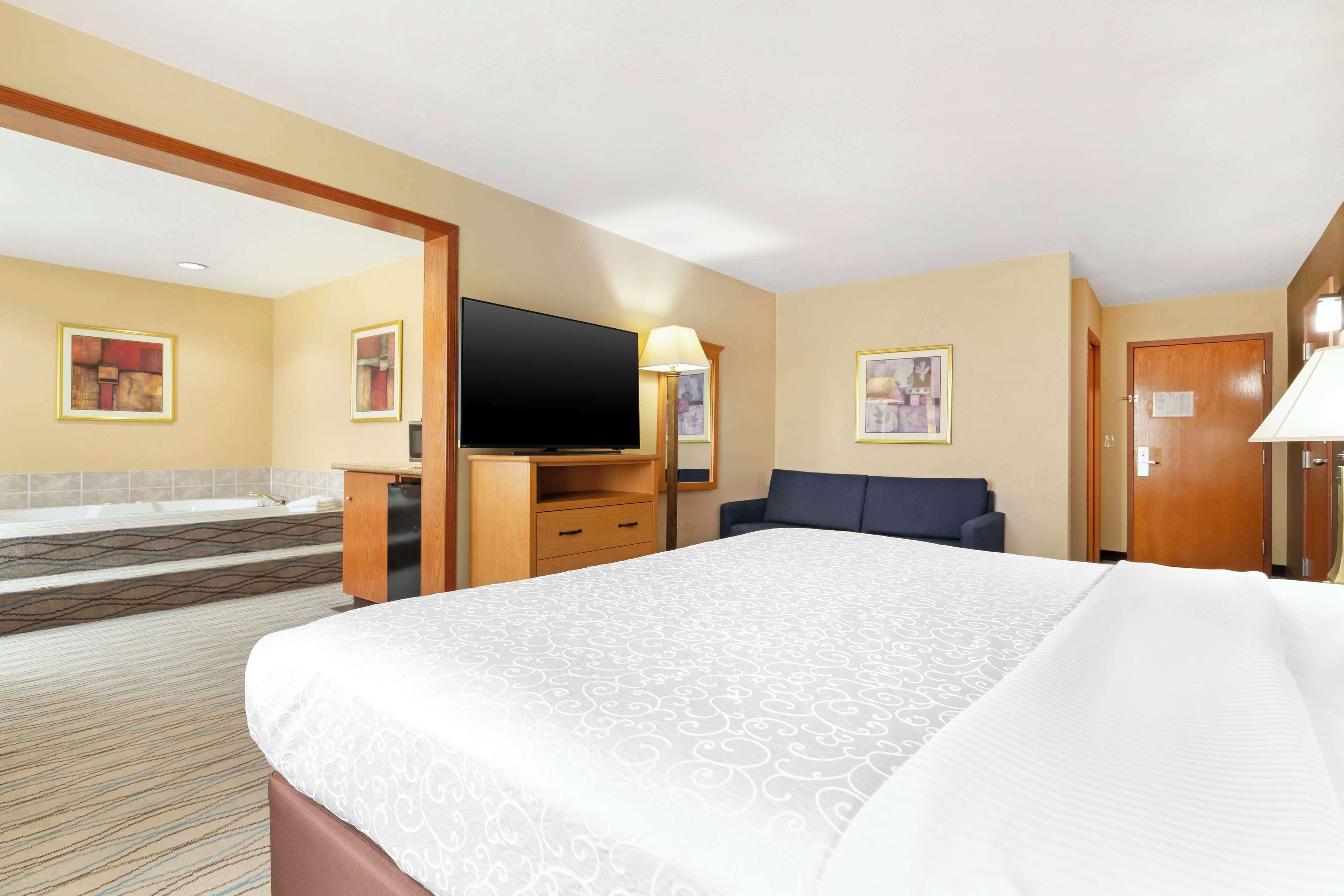 Una habitación de hotel con una cama grande, un televisor de pantalla plana, un escritorio con lámpara, un sofá y un baño con bañera.