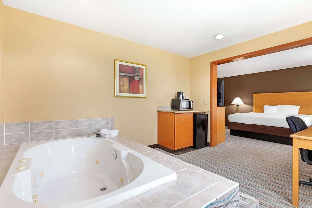 Ein Hotelzimmer mit einer großen Badewanne, einem Bett, einem Schreibtisch und einer Mikrowelle.