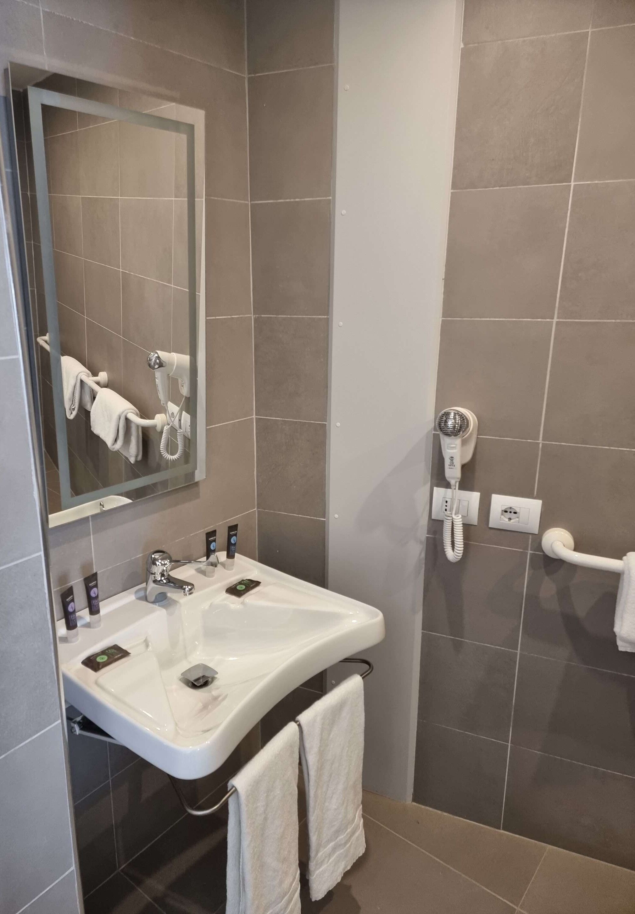 Une salle de bain équipée d’un lavabo, d’un miroir, d’un porte-serviettes et d’un sèche-cheveux fixé au mur.
