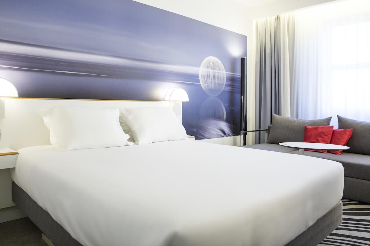 A hotel room with a large bed, a sofa, a small table, and a view of the sea.