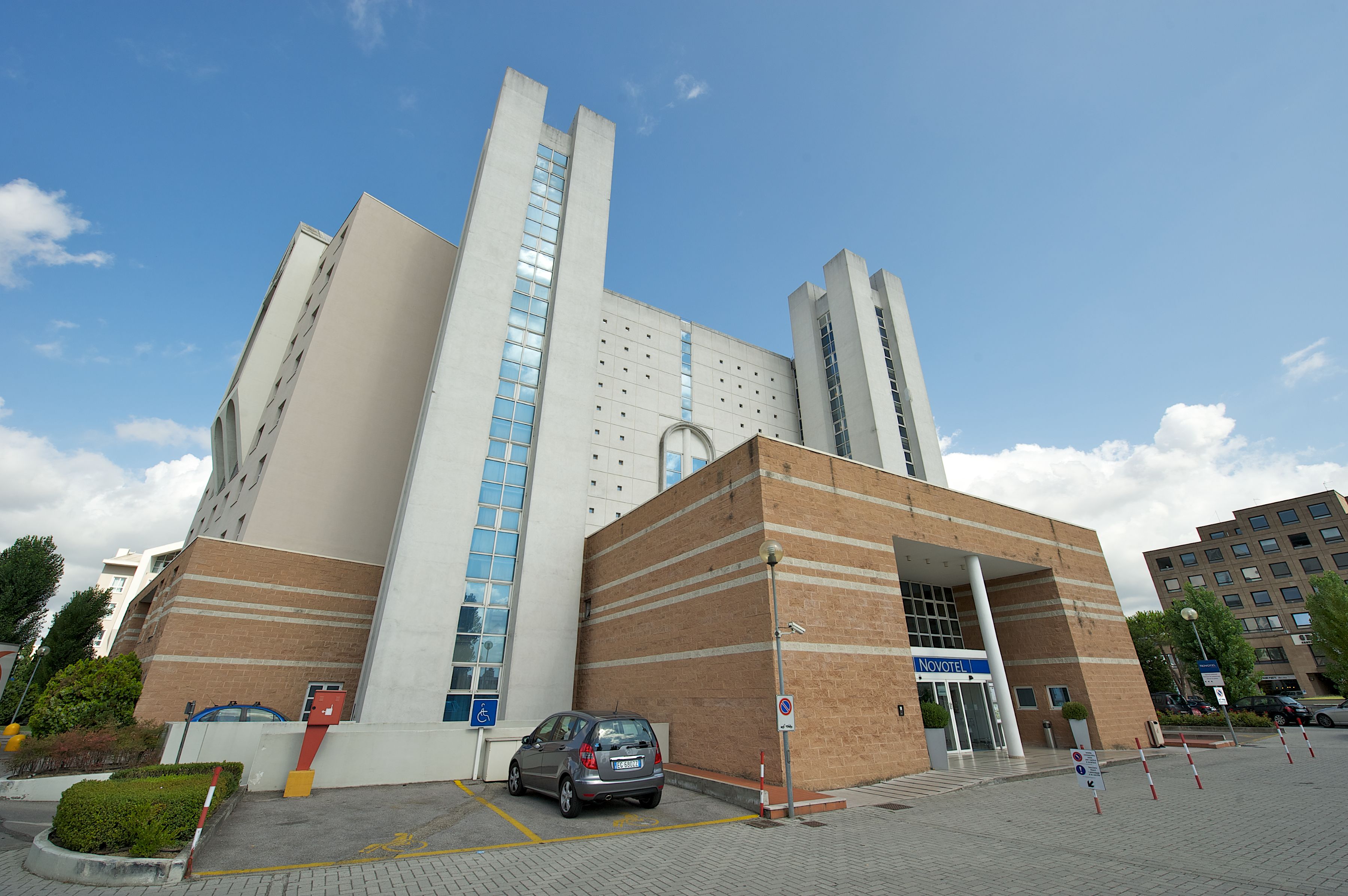 Ein modernes Gebäude mit einer markanten Eingangspartei, einem Parkplatz und einem strahlend blauen Himmel.