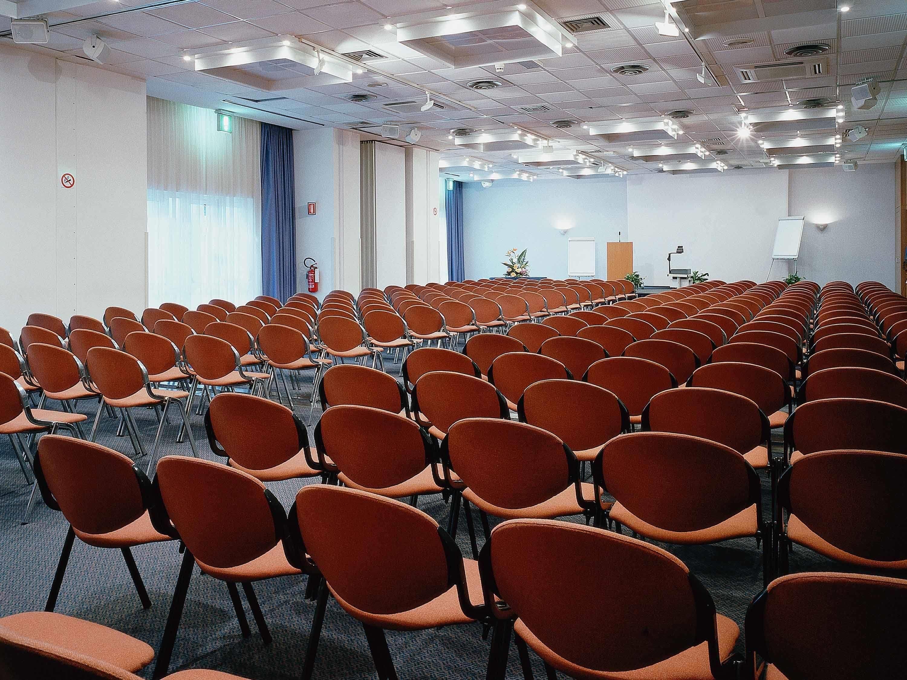 A conference room with rows of orange chairs, a podium, and a whiteboard.