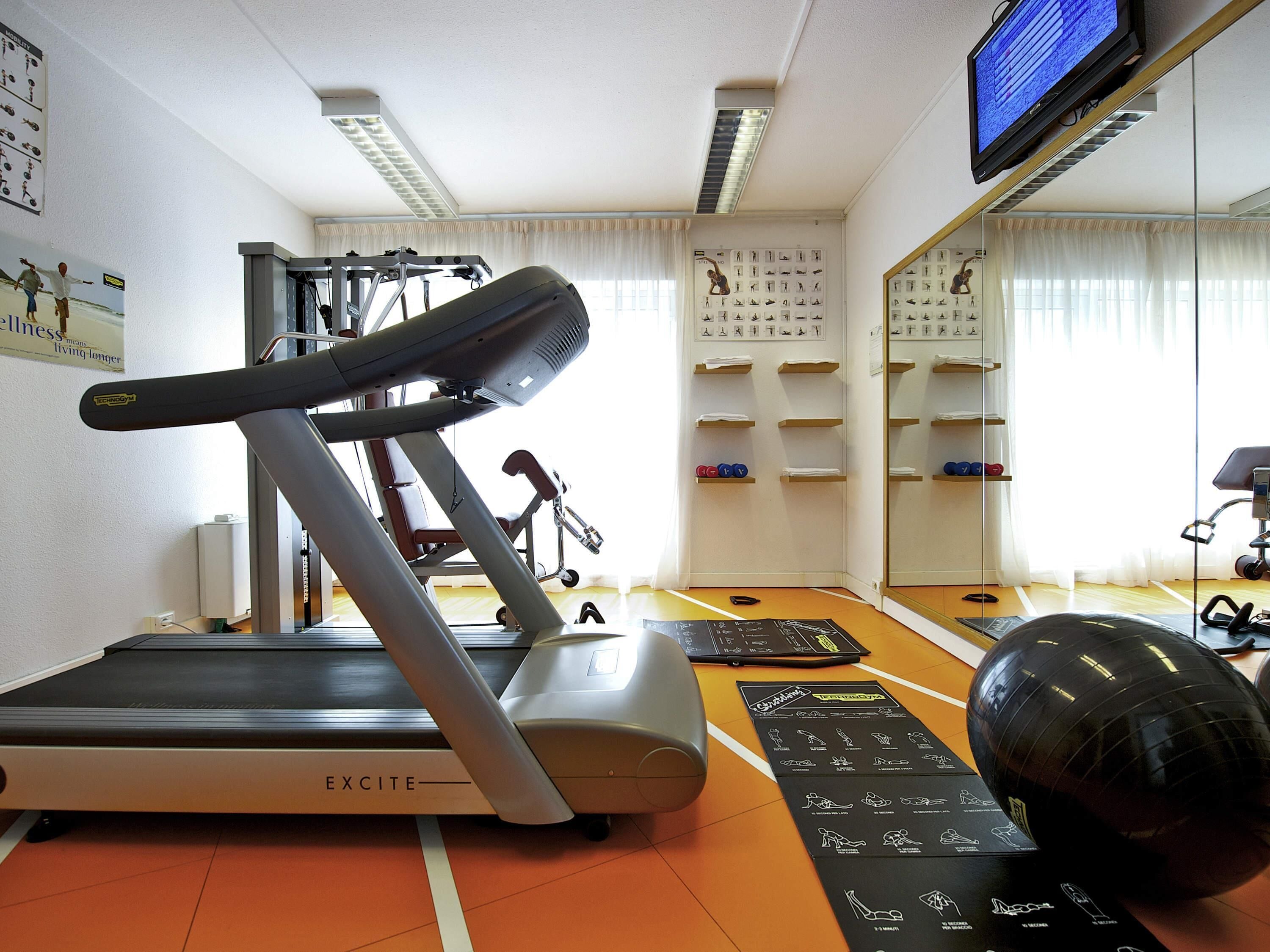 A gym with a treadmill, exercise equipment, a mirror, and a wall with fitness posters.