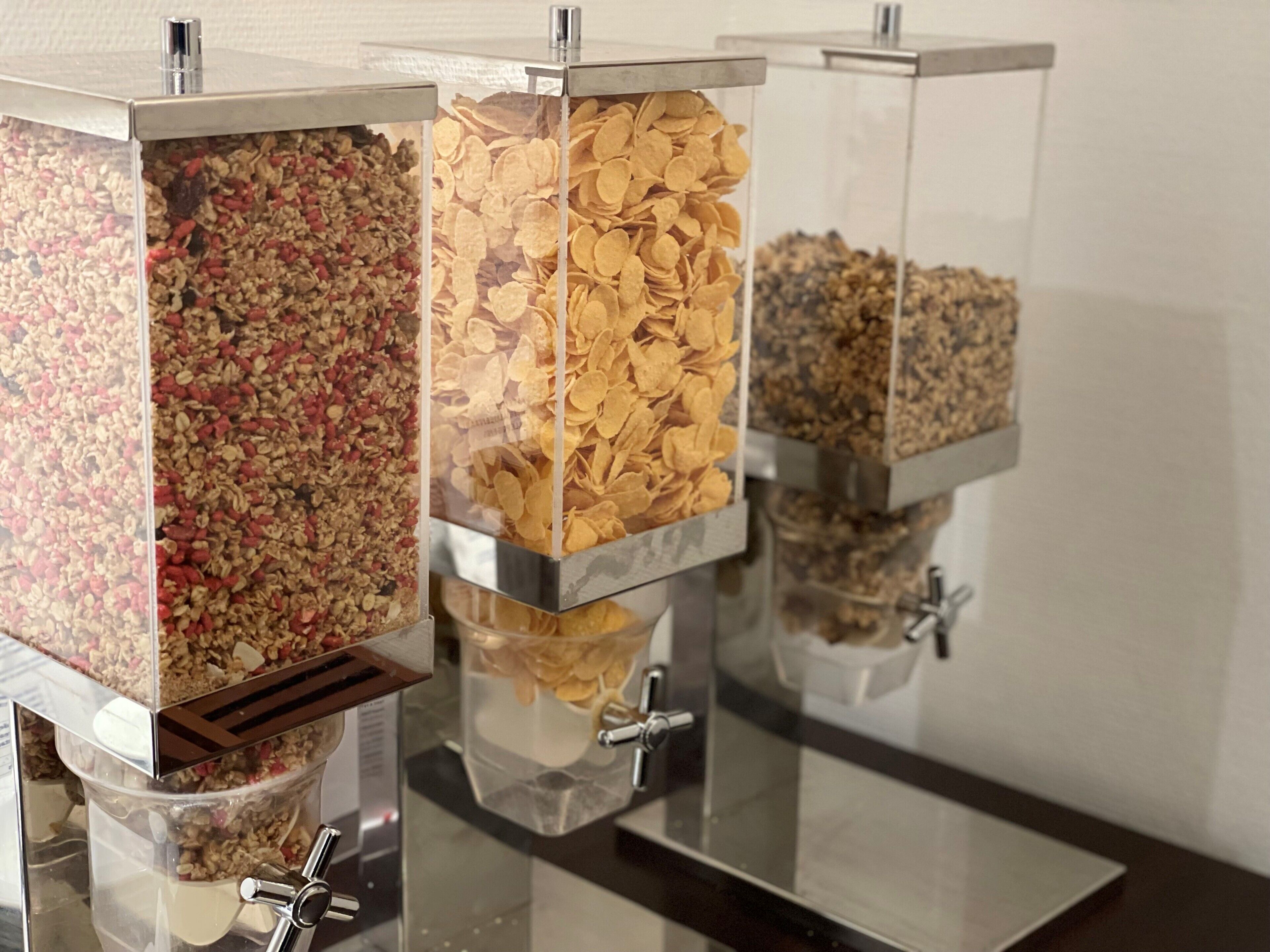 Tre distributori trasparenti con diversi tipi di granola e fiocchi di cereali.