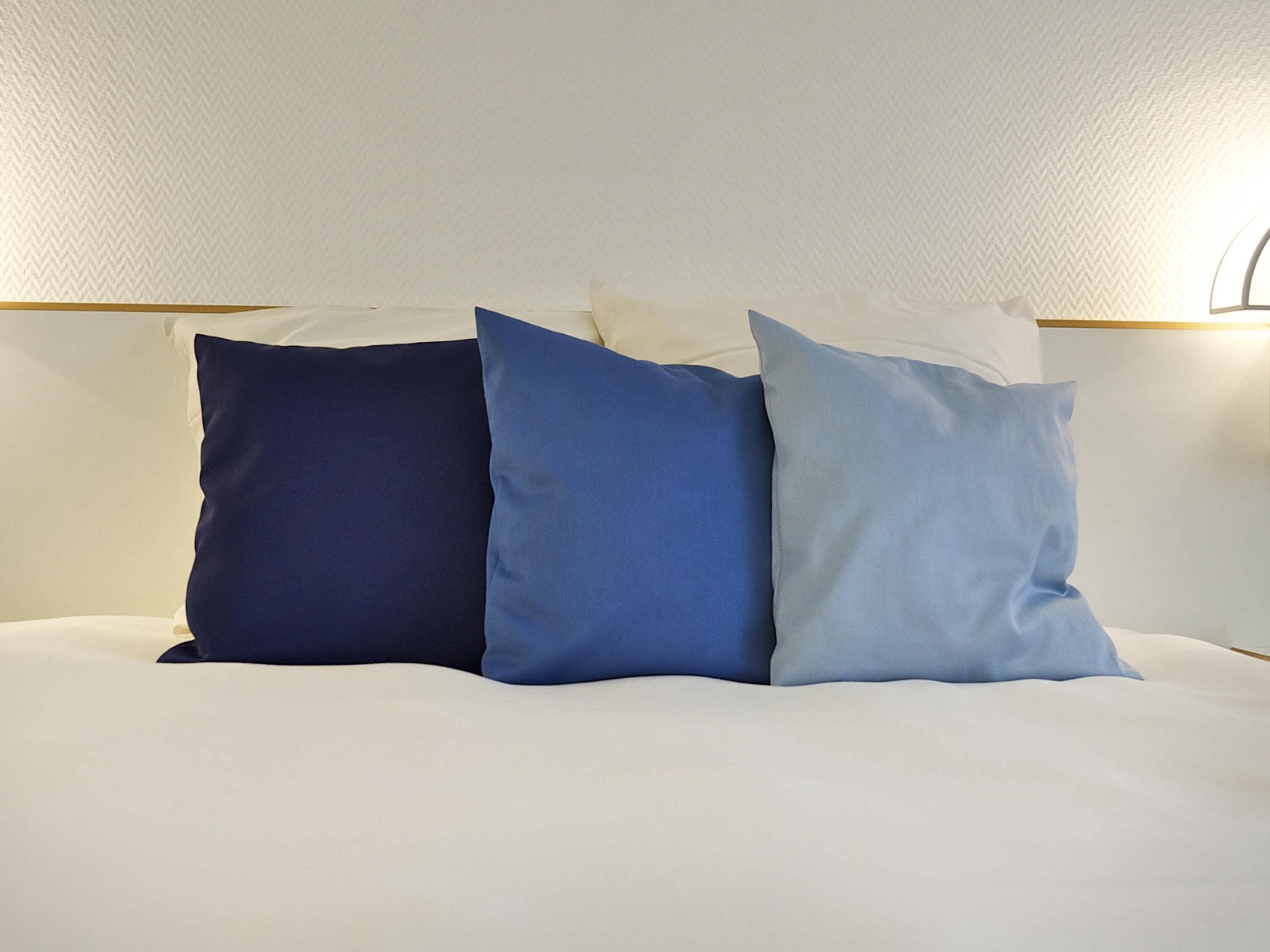 A bed with three pillows in shades of blue and white.