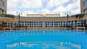 A swimming pool with a clear blue water surface, surrounded by a building with large windows and a flat roof. - Novotel Firenze Nord Aeroporto (Sesto Fiorentino)