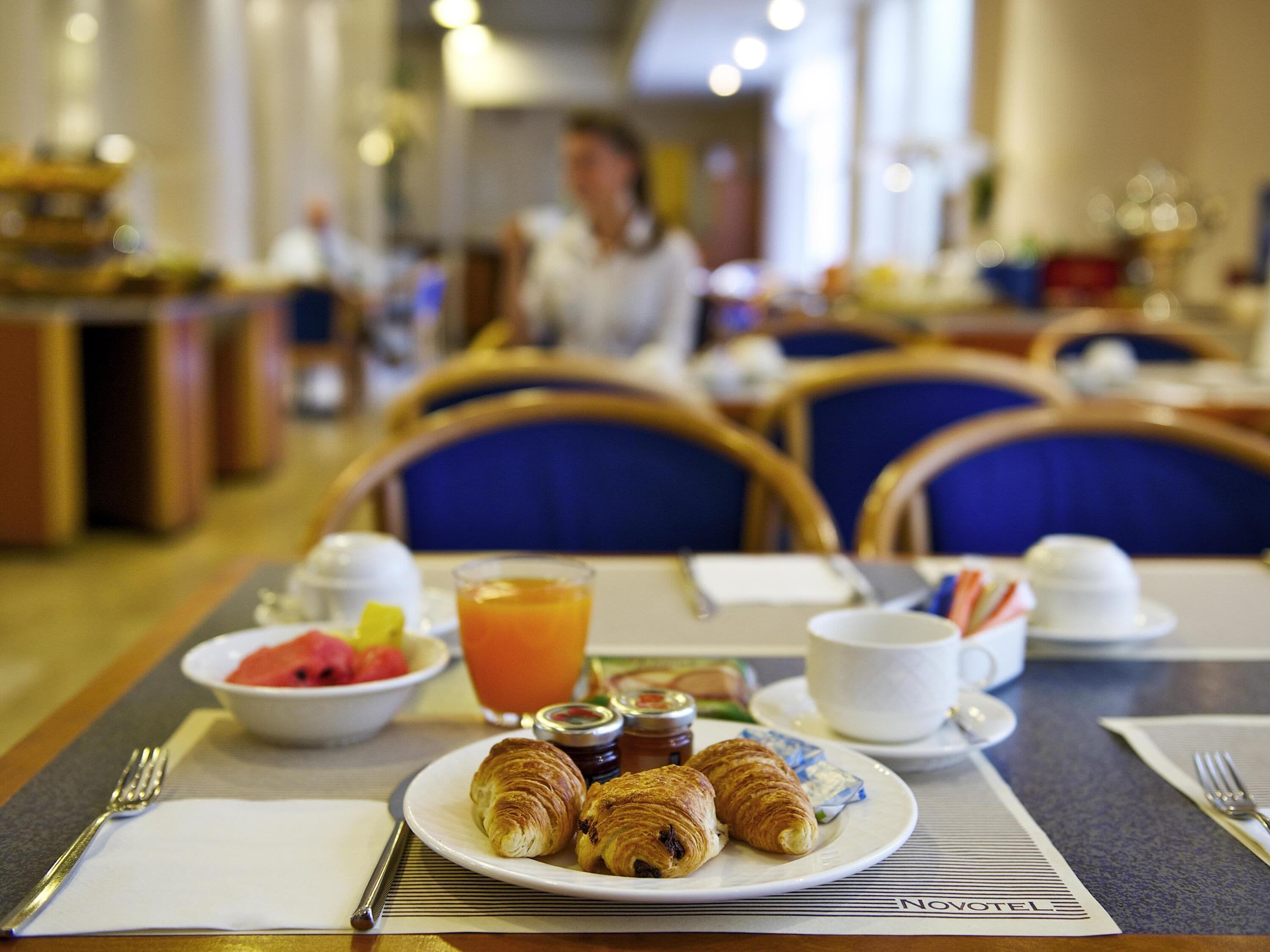 A breakfast setting with croissants, a bowl of fruit, and a glass of orange juice on a table.