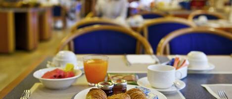 A breakfast setting with croissants, a bowl of fruit, and a glass of orange juice on a table.